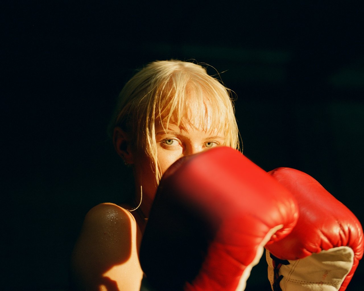 Boxer with wet blonde hair raising red gloves in a guard stance, eyes focused straight ahead